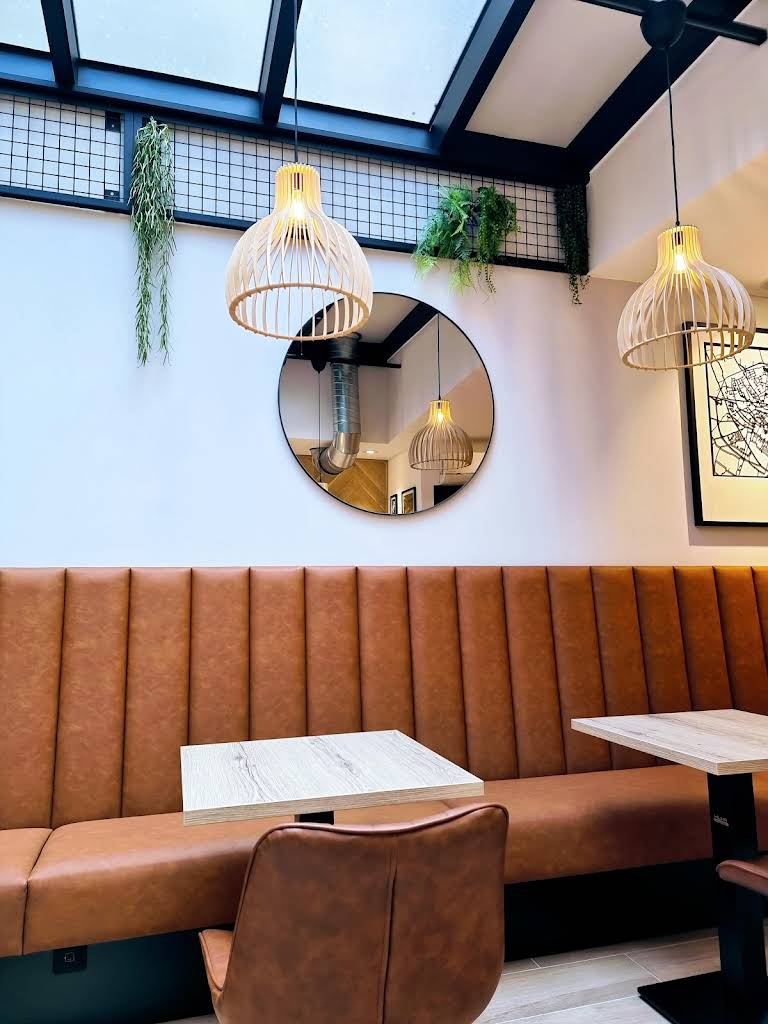 Espace café Leonidas Hazebrouck avec banquettes en cuir, verrière et suspensions en osier