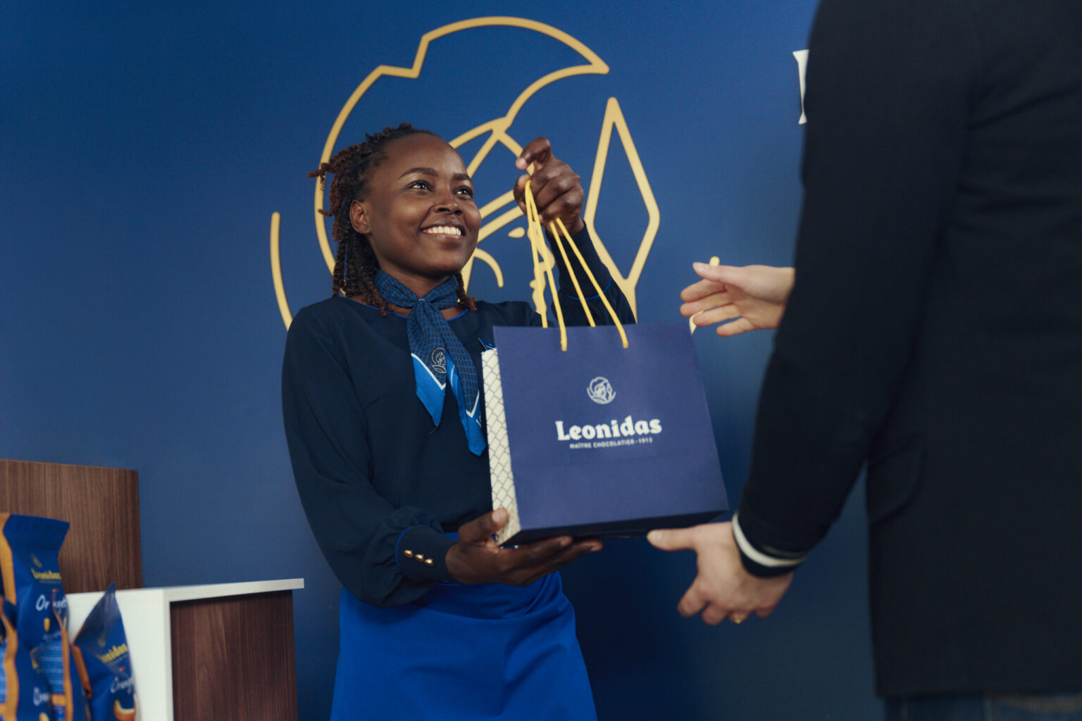Vendeuse Leonidas remettant un sac cadeau à une cliente en boutique