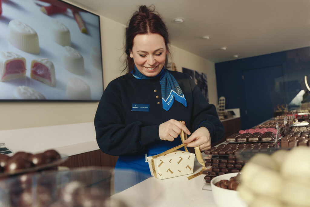 Chocolatière Leonidas nouant le ruban d'un ballotin derrière le comptoir